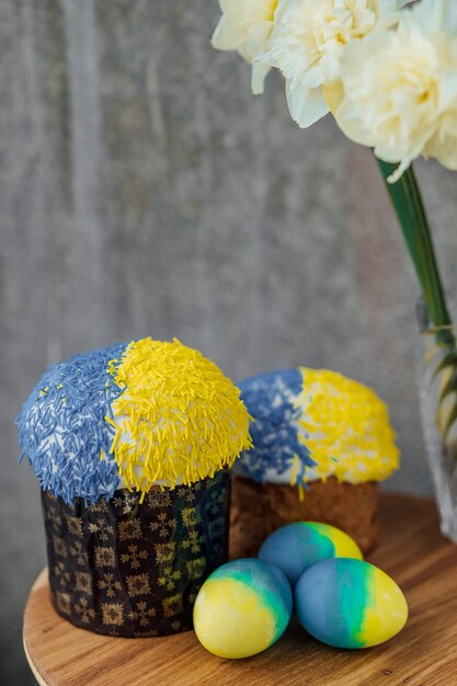 Deliziose torte pasquali nei colori della bandiera dell'Ucraina uova di Pasqua colorate in giallo blu su un tavolo di legno con fiori sullo sfondo posto per il fuoco selettivo del testo