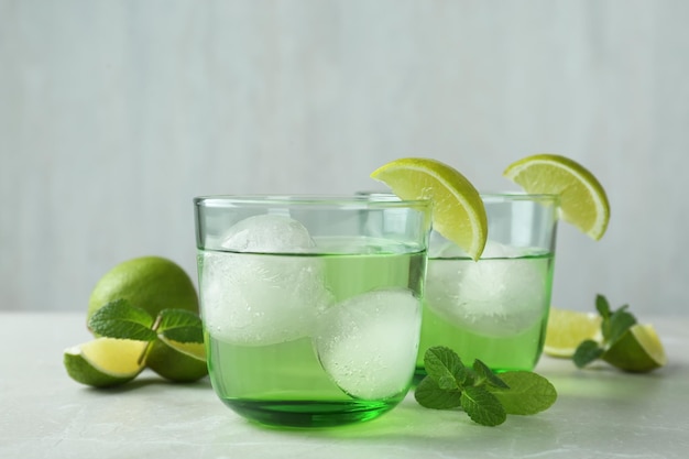 Deliziosi cocktail con lime e palline di ghiaccio sul tavolo grigio