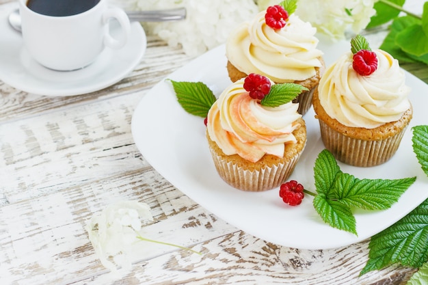 Deliziosi cupcakes alla vaniglia con panna e lamponi su un legno bianco