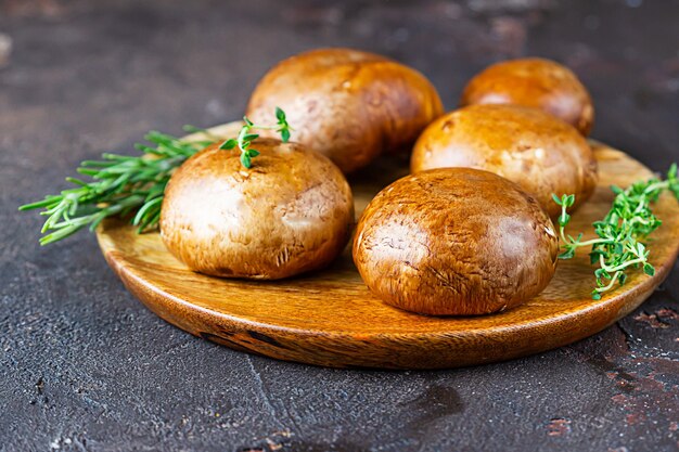 Deliziosi funghi portobello freschi con timo e rosmarino sul tagliere di legno.