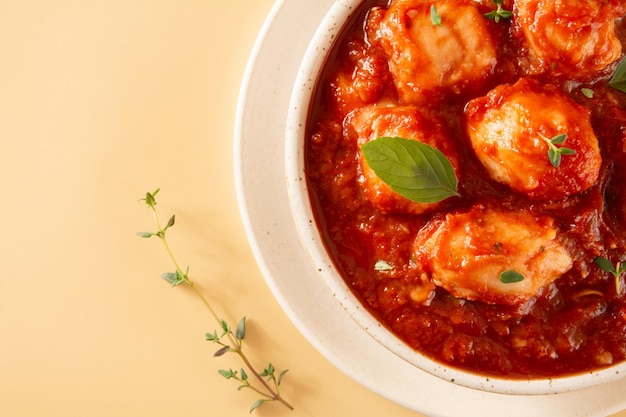 Deliziosi Gnocchi con Salsa Rossa e Basilico serviti in una Ciotola di Ceramica Fatta a Mano testurizzata Bianca in uno sfondo beige pulito con decorazione di timo in vista dall'alto ritagliata