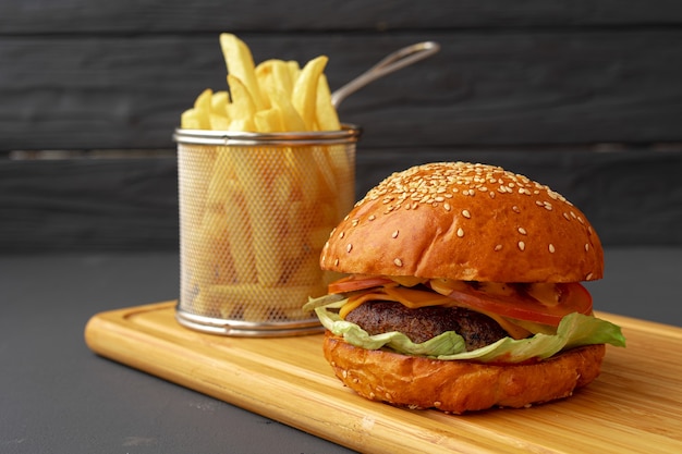 Deliziosi hamburger e patatine fritte sulla tavola di legno su sfondo nero