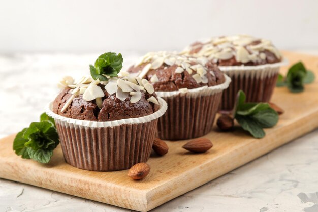 Deliziosi muffin al cioccolato dolci, con petali di mandorle accanto a menta e noci di mandorle su un tavolo di cemento leggero. avvicinamento