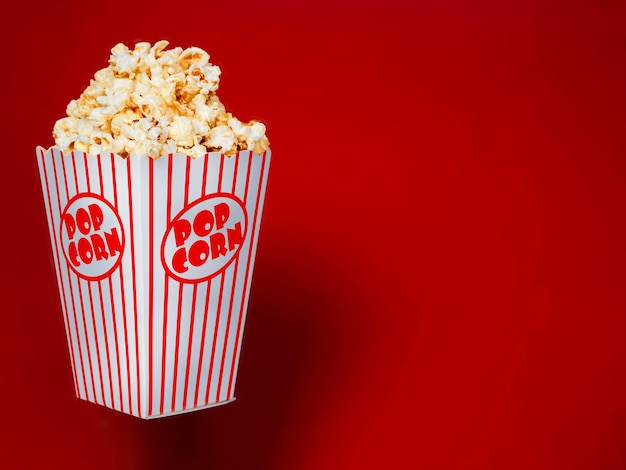 Deliziosi popcorn in una tazza di carta a strisce rosse su uno sfondo rosso Messa a fuoco selettiva