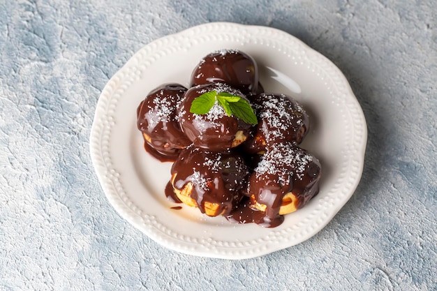 Deliziosi profiteroles con cioccolato e piatto bianco. Immagine di messa a fuoco selettiva su sfondo chiaro.