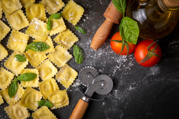 Deliziosi ravioli crudi con farina e basilico su fondo scuro. Il processo di produzione dei ravioli italiani.