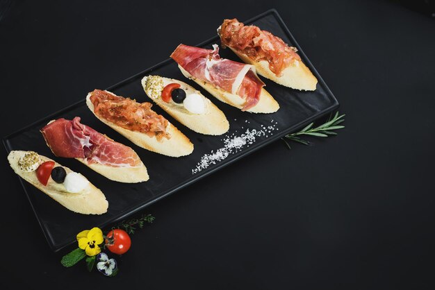 Deliziosi snack con prosciutto a forma di barchetta su sfondo nero. Copia spazio