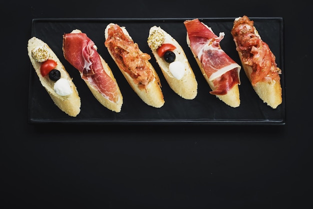 Deliziosi snack con prosciutto a forma di barchetta su sfondo nero. Copia spazio