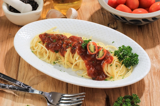 Deliziosi spaghetti serviti su piatto ovale bianco. Sulla tavola di legno