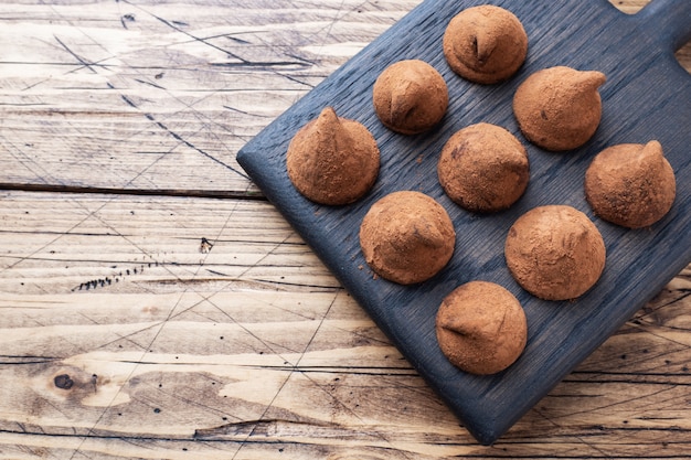 Deliziosi tartufi al cioccolato cosparsi di cacao in polvere su un supporto di legno. Fondo in legno Copia spazio.