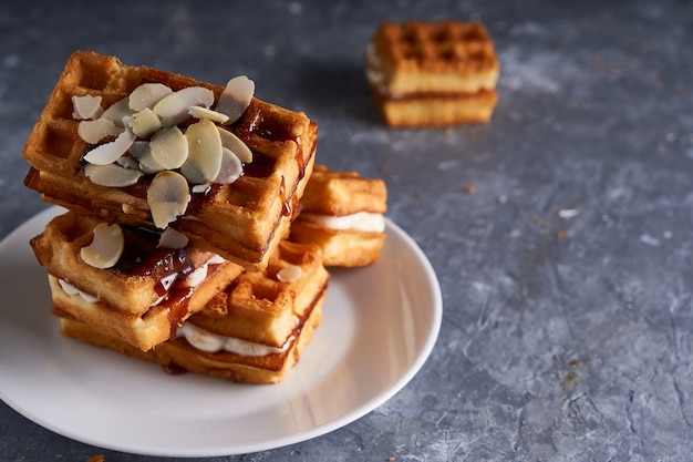 Deliziosi waffle fatti in casa di Vienna con sciroppo e mandorle briciole serviti su un tavolo grigio