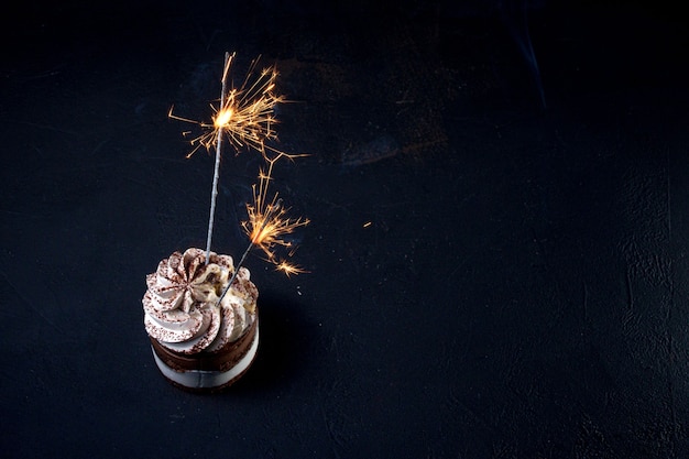 Delizioso bigné di compleanno con fuochi d'artificio candela sul tavolo su sfondo scuro