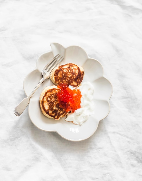 Delizioso brunch a colazione su uno sfondo chiaro pancake con crema acida e caviale rosso