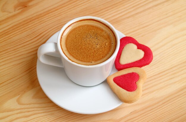 Delizioso caffè espresso schiumoso con un paio di biscotti a forma di cuore su un tavolo di legno