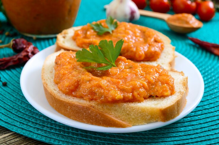 Delizioso caviale di zucca in un barattolo e spalmato su fette di pane bianco sul tavolo. Caviale fatto in casa con zucchine, aglio, carote, salsa di pomodoro. Cucina vegana. Avvicinamento