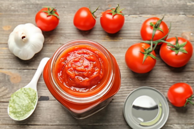 Delizioso concentrato di pomodoro in barattolo con ingredienti su sfondo di legno