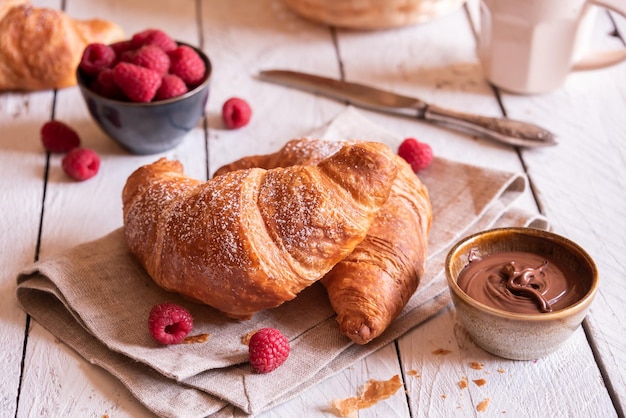 Delizioso croissant dolce con cioccolato e frutta sulla tavola di legno bianca