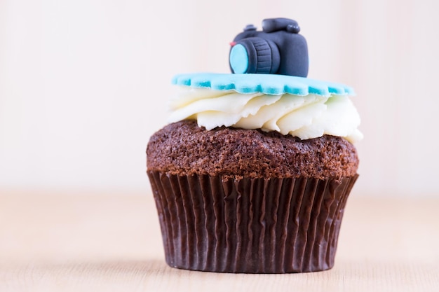 Delizioso cupcake con l'icona realistica della fotocamera su una scrivania in legno