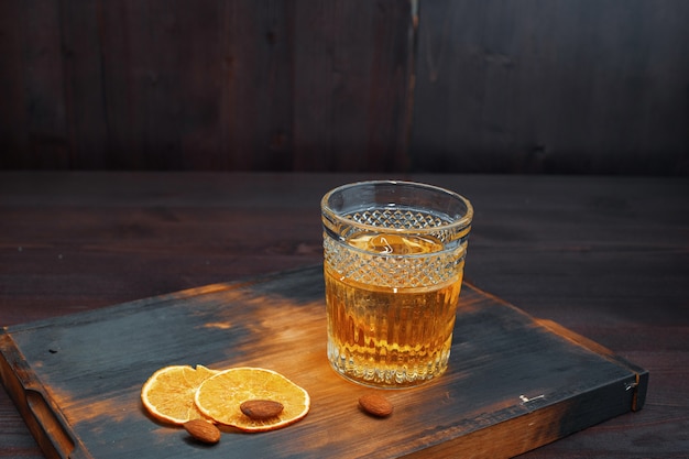 Delizioso e sorprendente whisky scozzese in un bicchiere di cristallo decorato con fette di arancia fresca si trova su un tavolo di legno vintage nel pub. Forte bevanda maschile. Fine settimana al bar