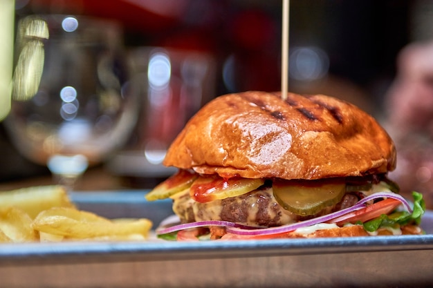 Delizioso hamburger alla griglia gustoso con carne di manzo, formaggio, pancetta e salsa sulla tavola di legno con lo spazio della copia. Mani che tengono hamburger con patatine fritte e birra. Gruppo di amici che mangiano fast food