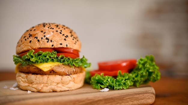 Delizioso hamburger di manzo con diapositive di pomodoro e lattuga su vassoio di legno su sfondo sfocato