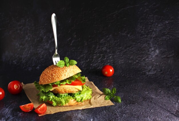 Delizioso hamburger fresco con cotoletta pomodori cetrioli formaggio e basilico su fondo scuro con una forchetta