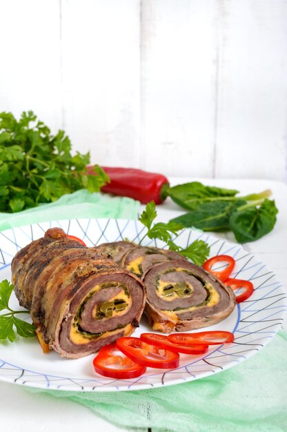 Delizioso involtino di carne con spinaci, formaggio e cetriolo sottaceto su un piatto su un fondo di legno bianco.