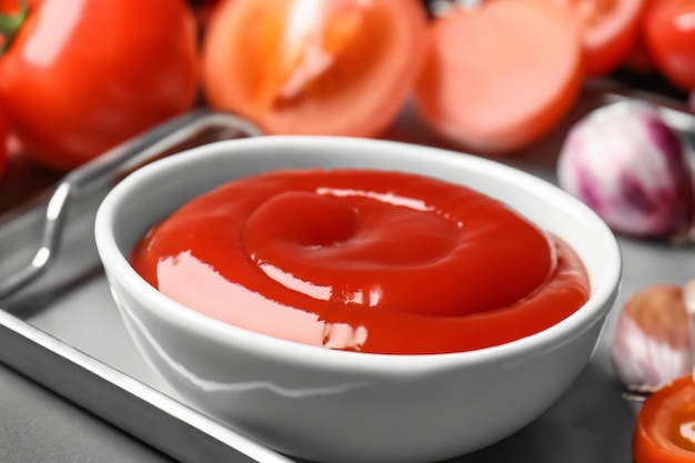 Delizioso ketchup in ciotola con ingredienti sul primo piano del vassoio