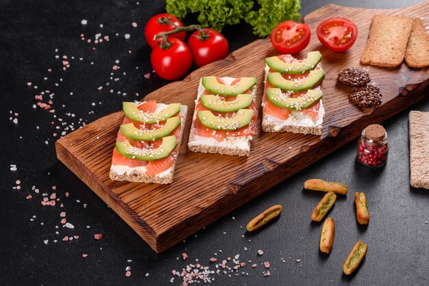 Delizioso panino fresco con pesce rosso, burro, pane e avocado su un tavolo di cemento scuro