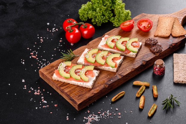Delizioso panino fresco con pesce rosso, burro, pane e avocado su un tavolo di cemento scuro