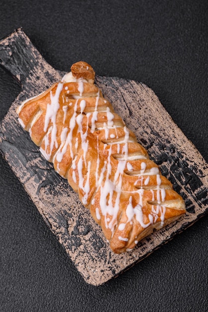 Delizioso panino intrecciato croccante con uvetta all'interno e glassa bianca all'esterno su uno sfondo di cemento scuro