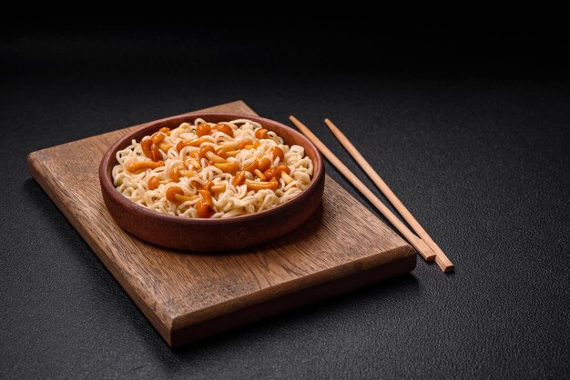 Delizioso piatto di cucina asiatica con spaghetti di riso, peperoni, funghi e spezie su uno sfondo di cemento scuro