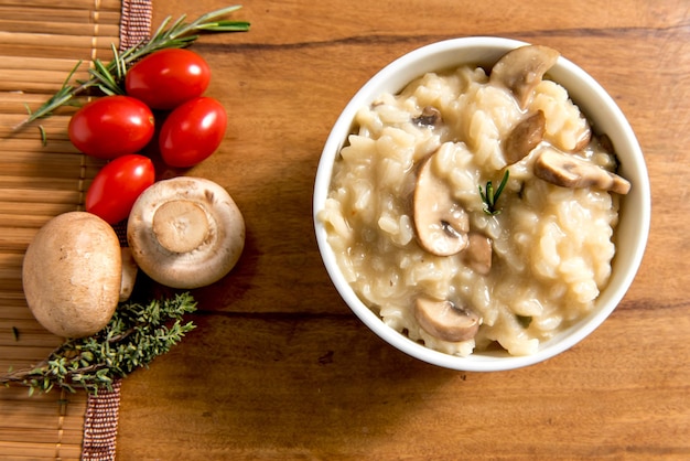 Delizioso piatto di risotto ai funghi su fondo di legno pomodorini ed erbe aromatiche