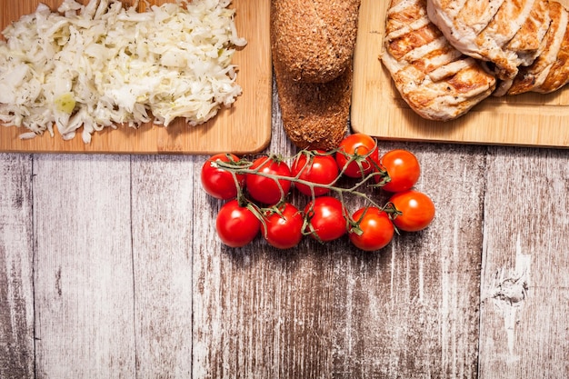 Delizioso pollo alla griglia su tavola di legno accanto a pane sano, pomodori e insalata. Stile di vita e alimentazione sani