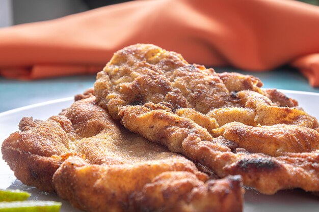 Delizioso pollo alla milanese pollo impanato con pangrattato e uovo un piatto tipico brasiliano Su un piatto bianco con pomodori limone su marmo blu