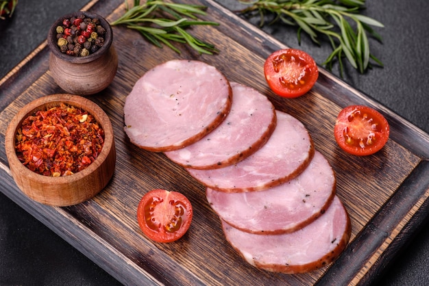 Delizioso prosciutto fresco tagliato a fette su un tagliere di legno su uno sfondo di cemento scuro