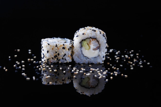 Delizioso rotolo di sushi con pesce e sesamo su uno sfondo nero con la riflessione Menu e ristorante