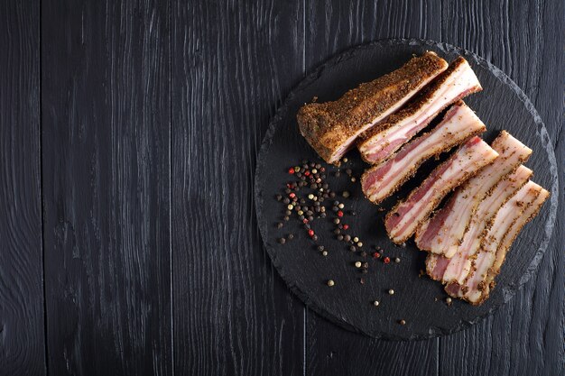 Delizioso speck affumicato speziato tagliato a fette su lastra di ardesia nera