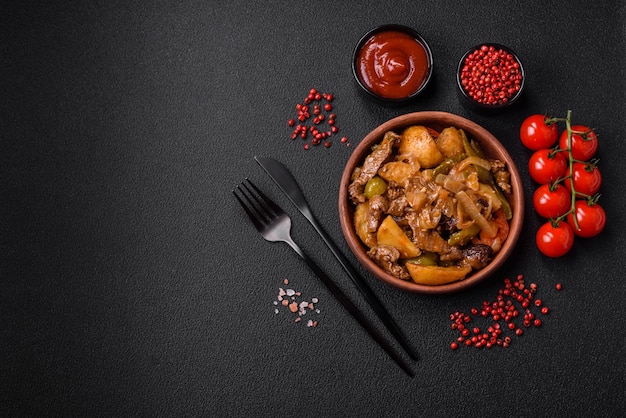 Delizioso stufato fresco di patate, pomodori, cipolle, carote e carne di manzo con sale, spezie ed erbe aromatiche su uno sfondo di cemento scuro