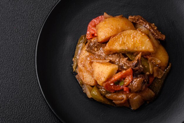 Delizioso stufato fresco di patate, pomodori, cipolle, carote e carne di manzo con sale, spezie ed erbe aromatiche su uno sfondo di cemento scuro