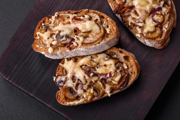 Delizioso toast croccante o bruschetta con funghi champignon di cipolla fritti e formaggio con spezie ed erbe aromatiche su uno sfondo di cemento scuro