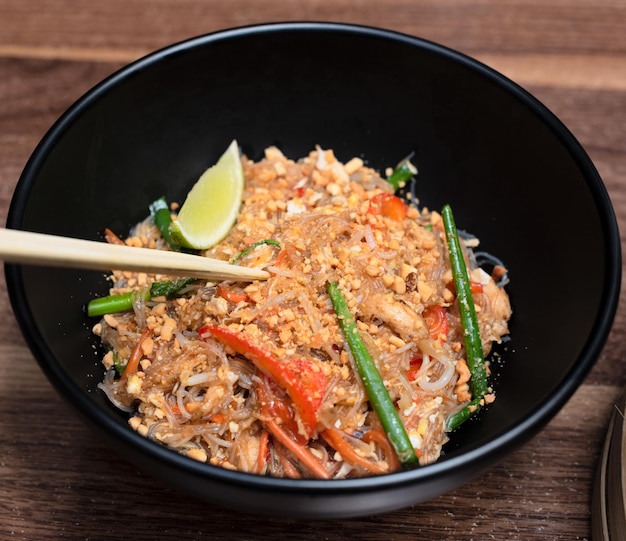 Delizioso wok di cibo asiatico con tagliatelle con bacchette su sfondo di legno Fuoco selettivo Concetto di cibo asiatico