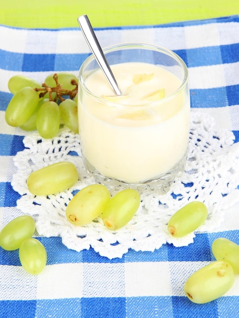 Delizioso yogurt in vetro con uva sulla tovaglia blu