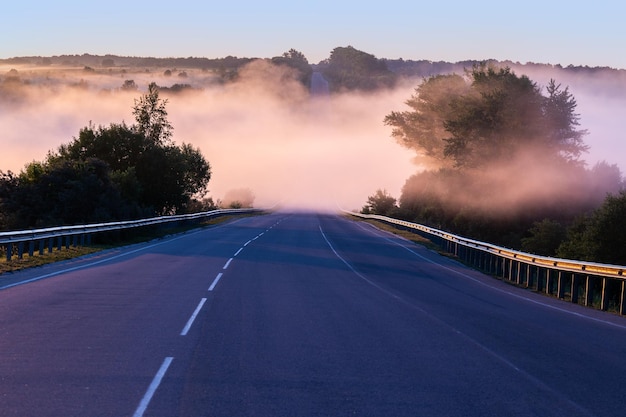 Dence nebbia mattutina nel mondo all'autostrada estiva vicino al fiume con ringhiere