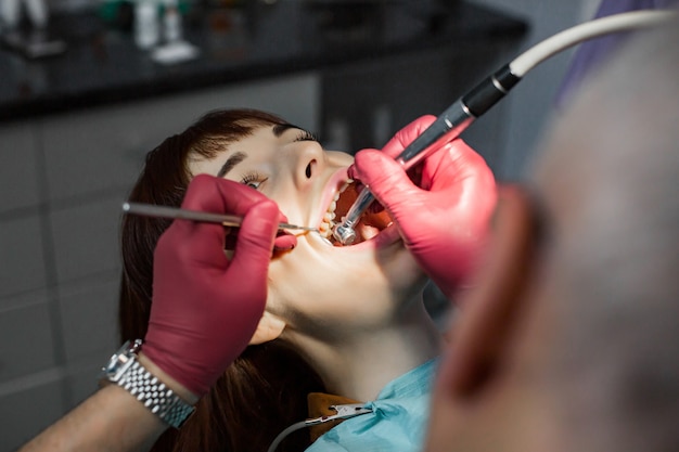 Dente di perforazione maschio senior del dentista al giovane paziente femminile in sedia dentaria