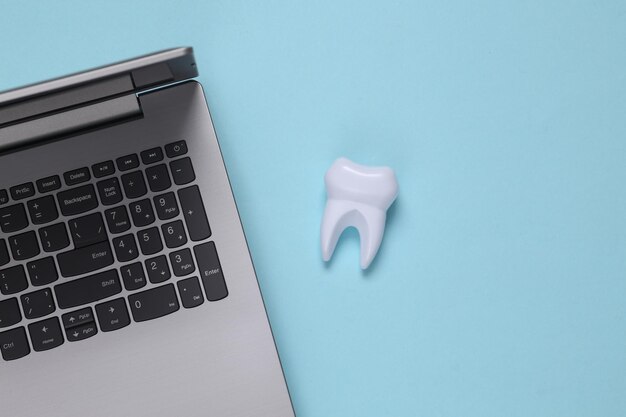 Dente falso e laptop su sfondo blu. Cura dei denti, concetto di medicina. Vista dall'alto