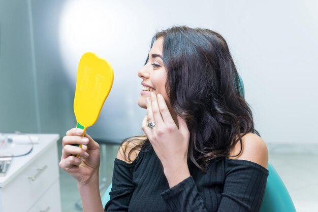 Denti di controllo femminile nello specchio Donna sorridente presso l'ufficio del dentista Sorridi più ampio e sii bello