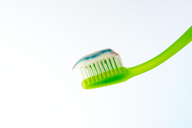 Dentifricio multicolore su uno spazzolino da denti verde su sfondo chiaro