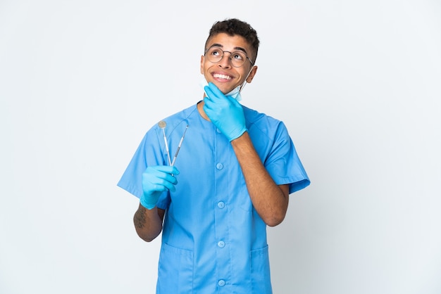 Dentista brasiliano che tiene strumento isolato sulla parete bianca che osserva in su mentre sorride