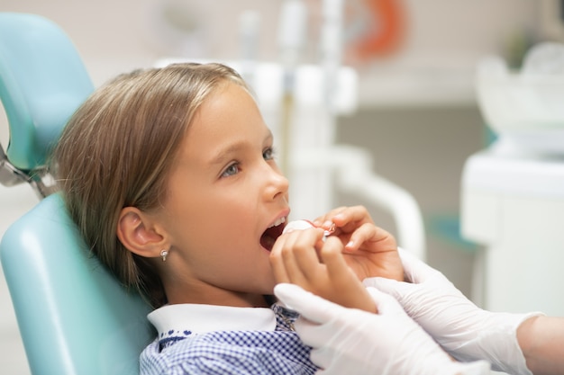 Dentista che aiuta. Utile dentista per bambini che indossa guanti bianchi che aiuta la ragazza a mettere il paradenti